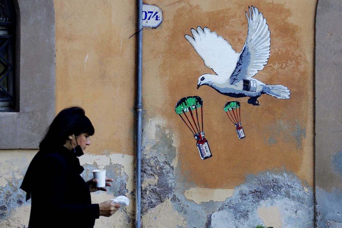 FILE - A woman walks past a mural depicting a white dove parachuting COVID-19 vaccine vials, posted near the Italian Health Ministry Headquarters in Rome, April 4, 2021. The pandemic is again roaring across parts of Western Europe, a prosperous region with relatively high vaccination rates and good health care systems but where lockdown measures to rein in the virus are largely a thing of the past. Italy, an early victim of the pandemic, has a high vaccination rate, but is also seeing numbers edge higher, which experts believe is due to vaccine efficacy wearing off. (Gregorio Borgia)