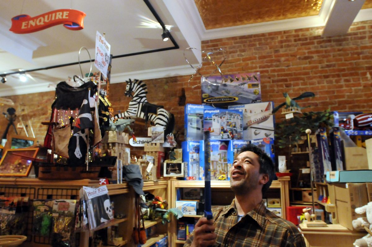 Brett Sommers of Figpickel’s Toy Emporium uses a static electricity wand to suspend a foil web in the air in the store in Coeur d’Alene.  (JESSE TINSLEY photos / The Spokesman-Review)