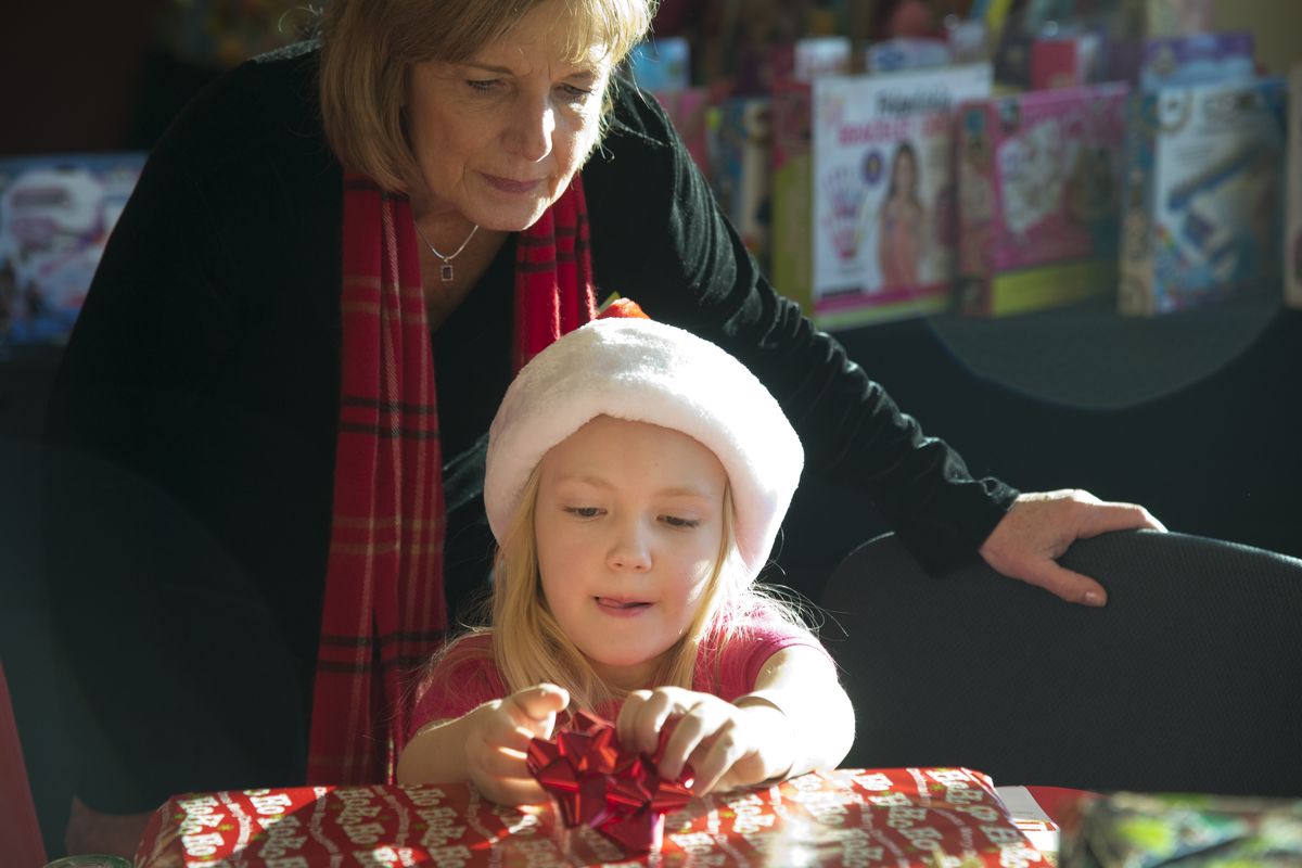 Ava Vanderhoes, 7, puts a bow on a present for a family member Monday with the help of Patti Petersen, who works in administration at Providence Sacred Heart Medical Center. In the center’s Children’s Hospital, patients and siblings had the opportunity to shop for and wrap gifts for visiting family members. (Jesse Tinsley)