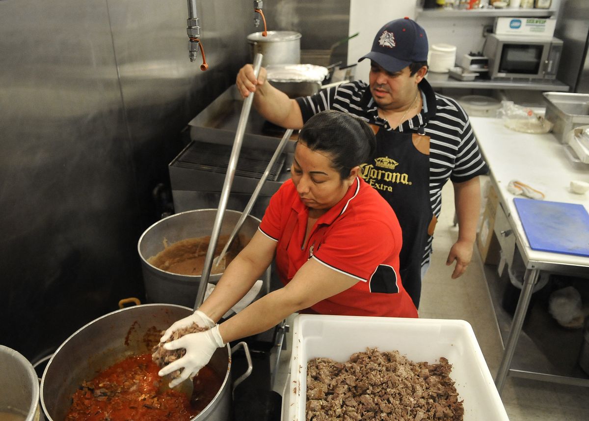 Maria Mendez adds beef to a pot of lard and pureed guajillo peppers  while Mario De Leon keeps the pot stirred at De Leon Foods in north Spokane.  (Photos by Dan Pelle / The Spokesman-Review)
