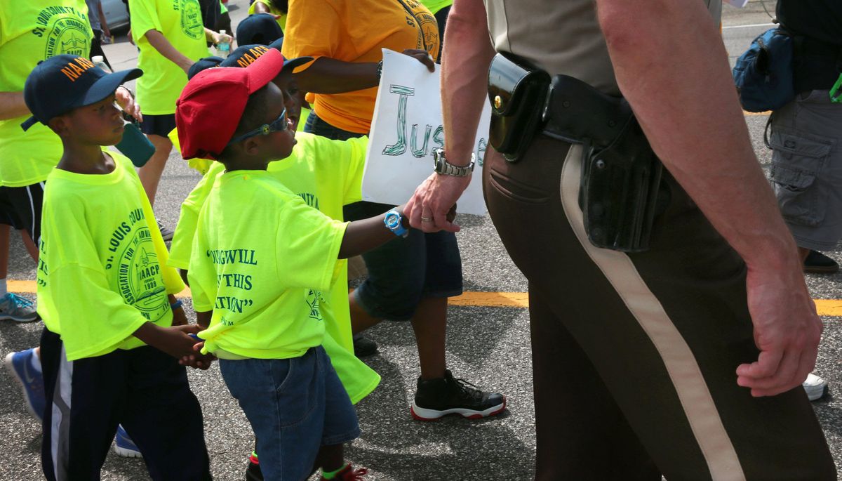 St. Louis County police Sgt. Colby Dolly joins hands with 5-year-old Zion King Frenchie during a march by members of the St. Louis chapters of the NAACP and the National Urban League in Ferguson, Mo., on Saturday. (Associated Press)