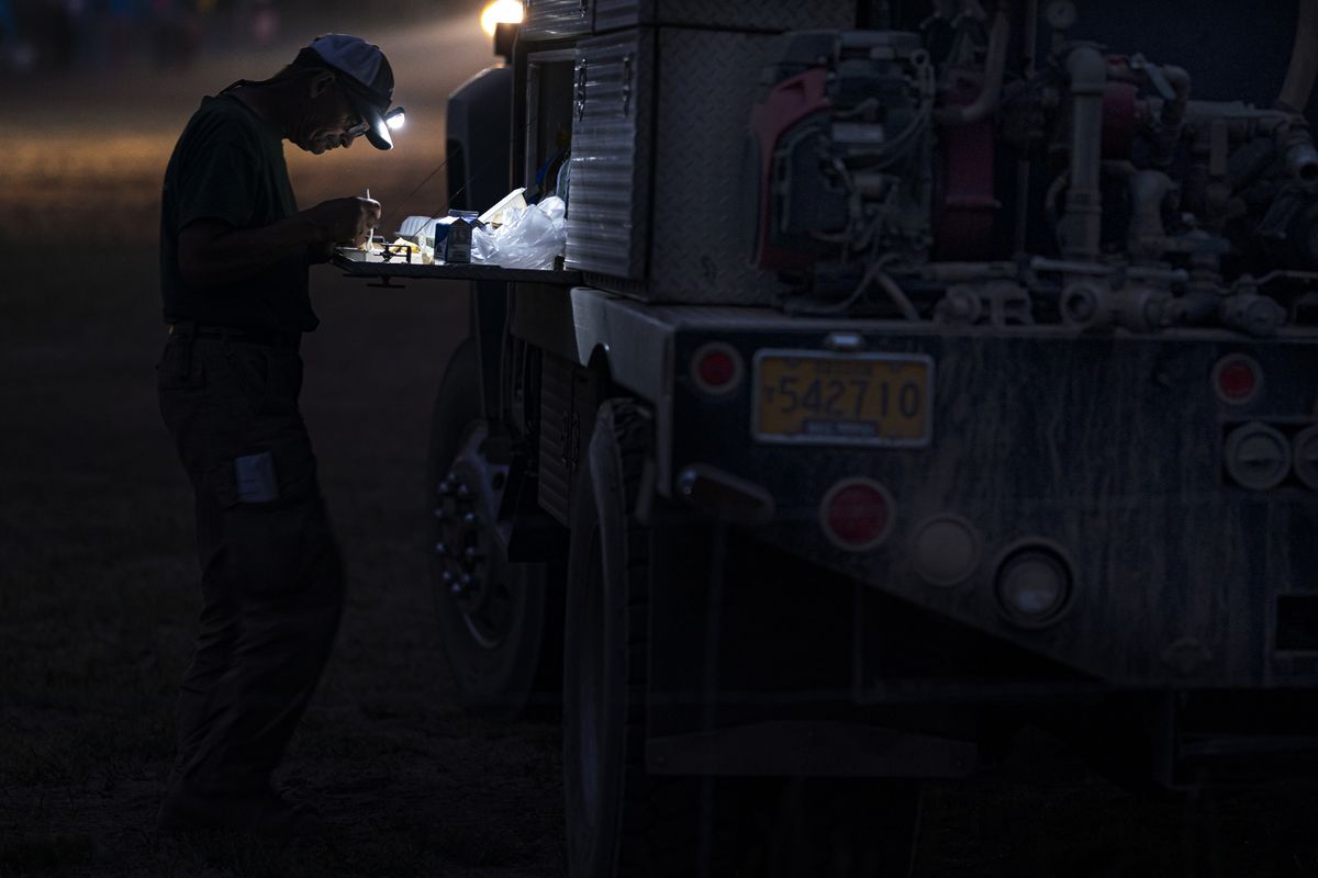 Firefighter Gary Robinson, with Pacific Habitat and Fire, eats dinner by headlamp after a 12-hour shift fighting the Bootleg Fire, late Tuesday, July 13, 2021, in Bly, Ore.  (Nathan Howard)