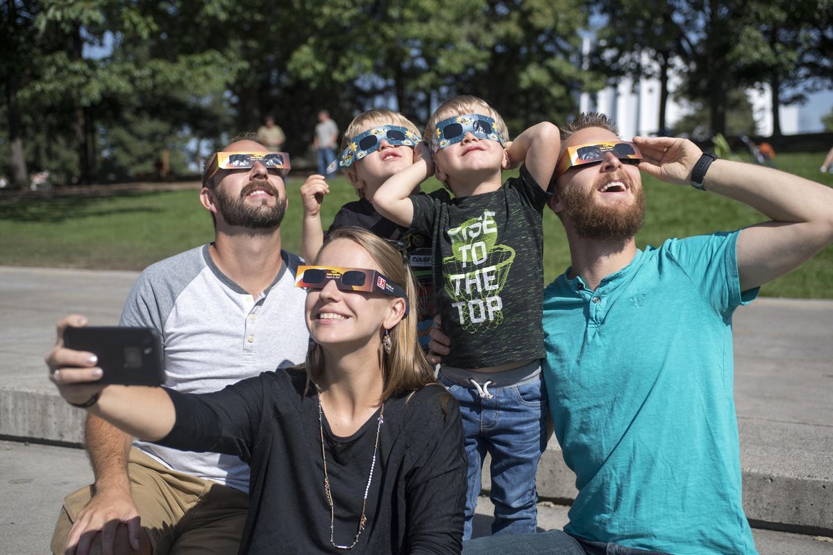 Kolie Sheehan holds her cellphone to make the perfect group photo of her twin sons Rhyder and Caylen, age 3, her husband Josh Sheehan, right, and family friend Brandon Erickson, left, during the partial solar eclipse in Spokane, Monday, Aug. 20, 2017. The Sheehan family is visiting from Shreveport, Louisiana. (Jesse Tinsley / The Spokesman-Review)