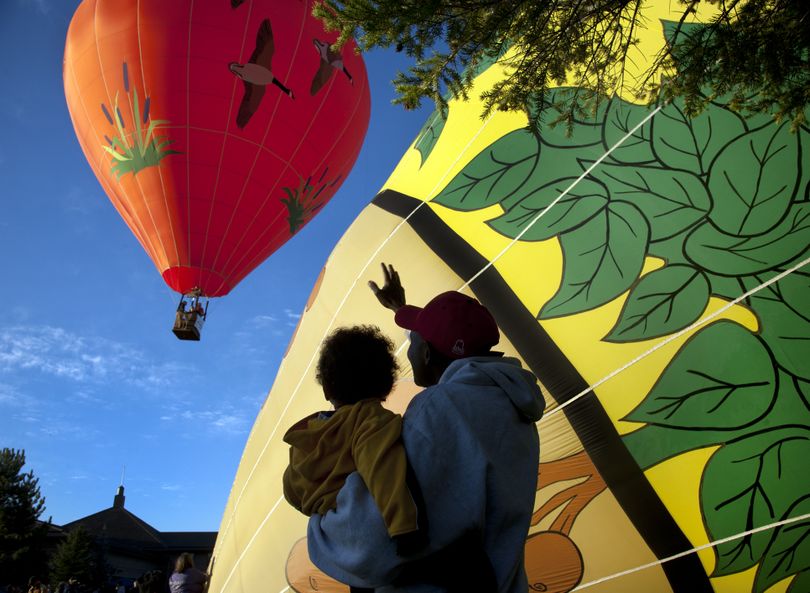 Geoffrey Mwangi and his son, Judah, 15 months, wave goodbye to the Wild Goose hot air balloon as the Spuds balloon inflates early Saturday morning during Valleyfest at CenterPlace in Spokane Valley. (PHOTOS BY DAN PELLE)
