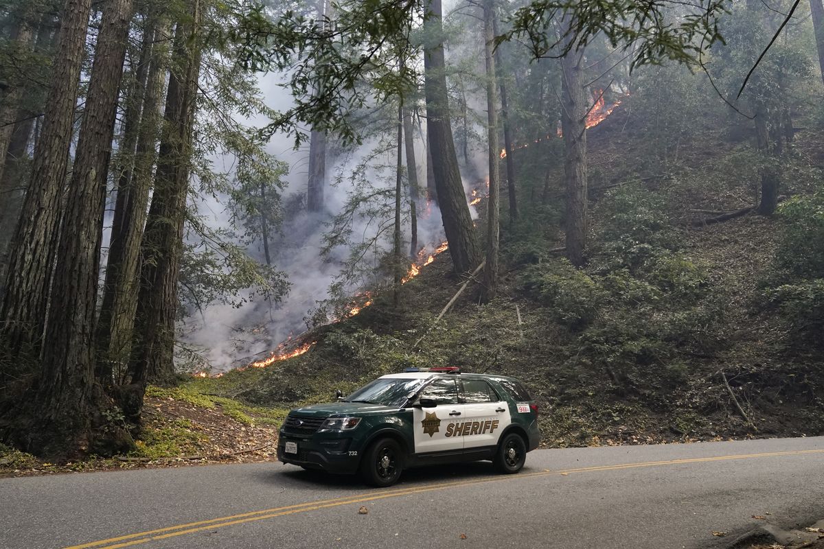 A police vehicle is seen under a forest being burned by the CZU August Lightning Complex Fire Monday, Aug. 24, 2020 near in Bonny Doon, Calif. (Marcio Jose Sanchez)