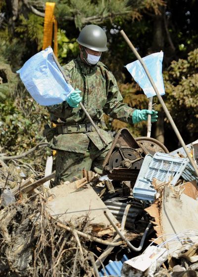 A Japan Self-Defense Force member places blue flags amid the rubble to signify that the place was already searched in Yamamoto, northern Japan, today. (Associated Press)