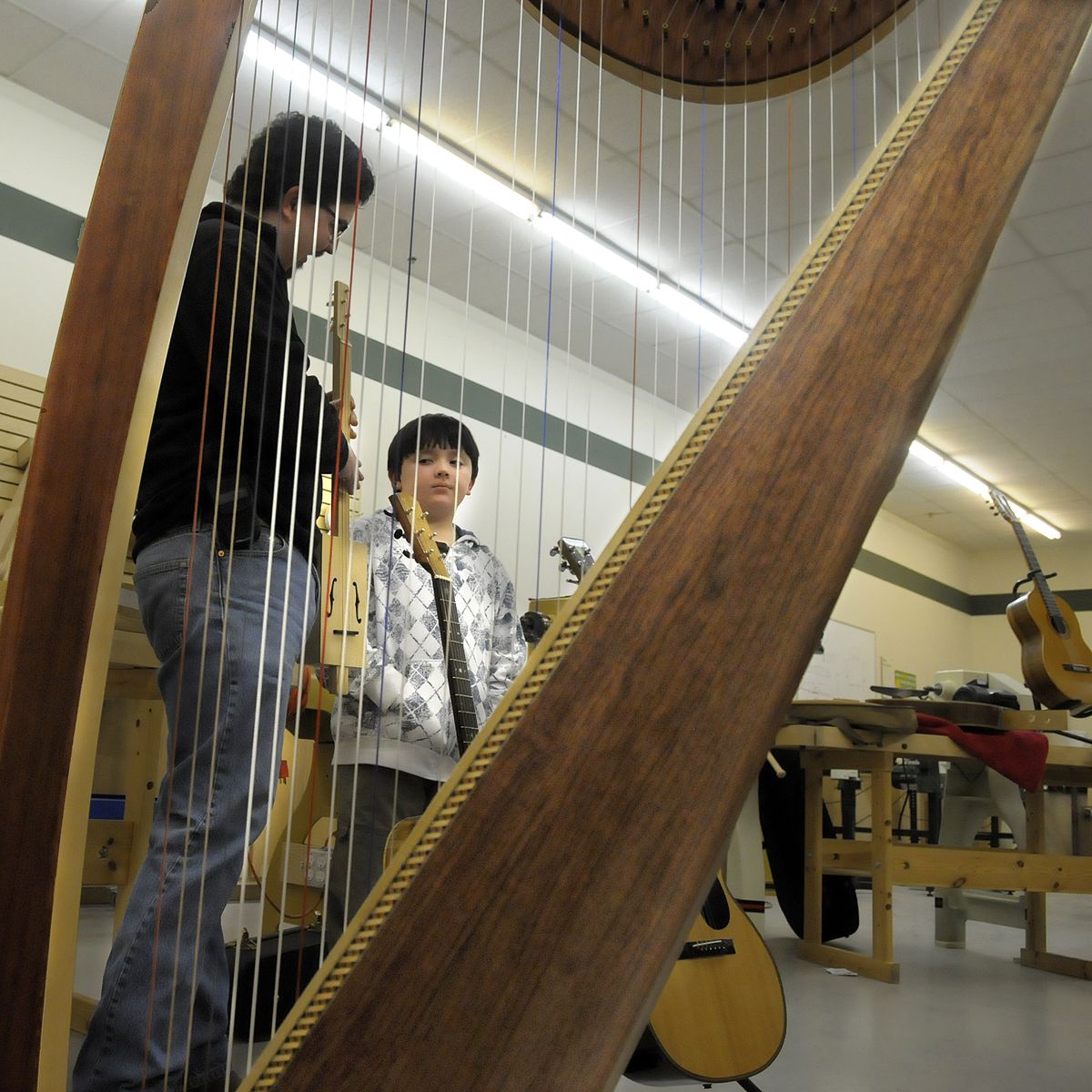 Mike, left, and Joey Conklin are framed in a handmade harp as they show off the cigarbox guitar Joey made recently. The father and son team were explaining their work last month at the Inland Northwest Luthiers Association show and tell meeting. (Christopher Anderson / The Spokesman-Review)