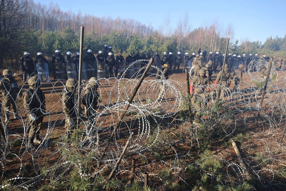 Polish police and border guards stand near the barbed wire as migrants from the Middle East and elsewhere gather at the Belarus-Poland border near Grodno Grodno, Belarus, Tuesday, Nov. 9, 2021. Hundreds if not thousands of migrants sought to storm the border from Belarus into Poland on Monday, cutting razor wire fences and using branches to try and climb over them. The siege escalated a crisis along the European Union