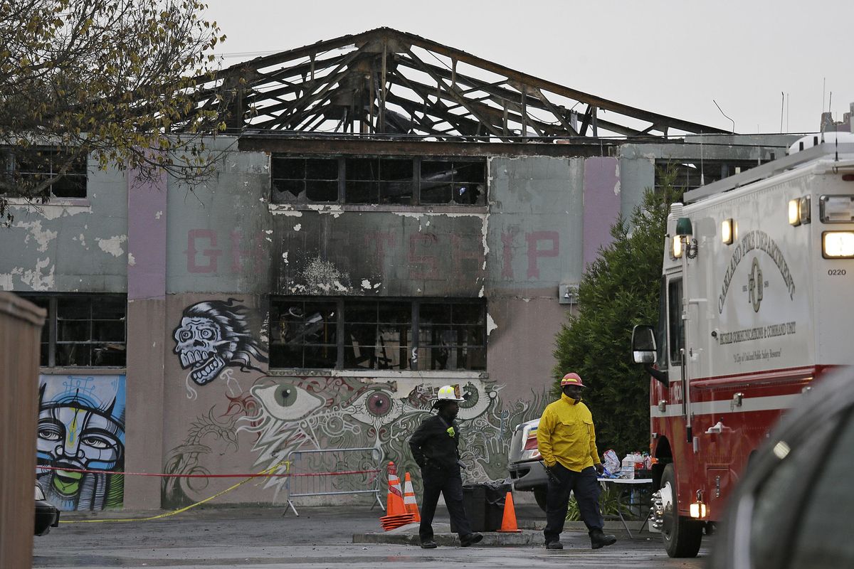This Dec. 7, 2016, file photo shows Oakland fire officials walk past the remains of the Ghost Ship warehouse damaged from a deadly fire in Oakland, Calif. (Eric Risberg / Associated Press)