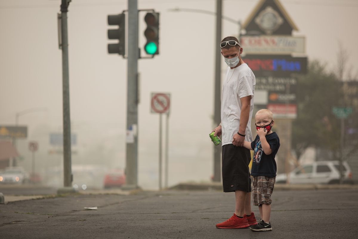 Cameron Bower, age 3, holds his dad Patrick Bower’s hand as they wait for a bus near Bridgeport Avenue and Division Street on Sunday in Spokane. The air quality was hazardous and hovered just below 500 ppm at the time.  (Libby Kamrowski/The Spokesman-Review)