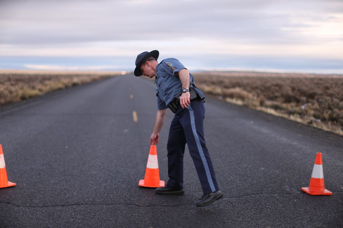 In a Jan. 28, 2016 file photo, an officer with the Oregon State Police moves a cone to establish a roadblock along one of the routes to the Malheur National Wildlife Refuge in Harney County, Ore. (Beth Nakamura / Associated Press)
