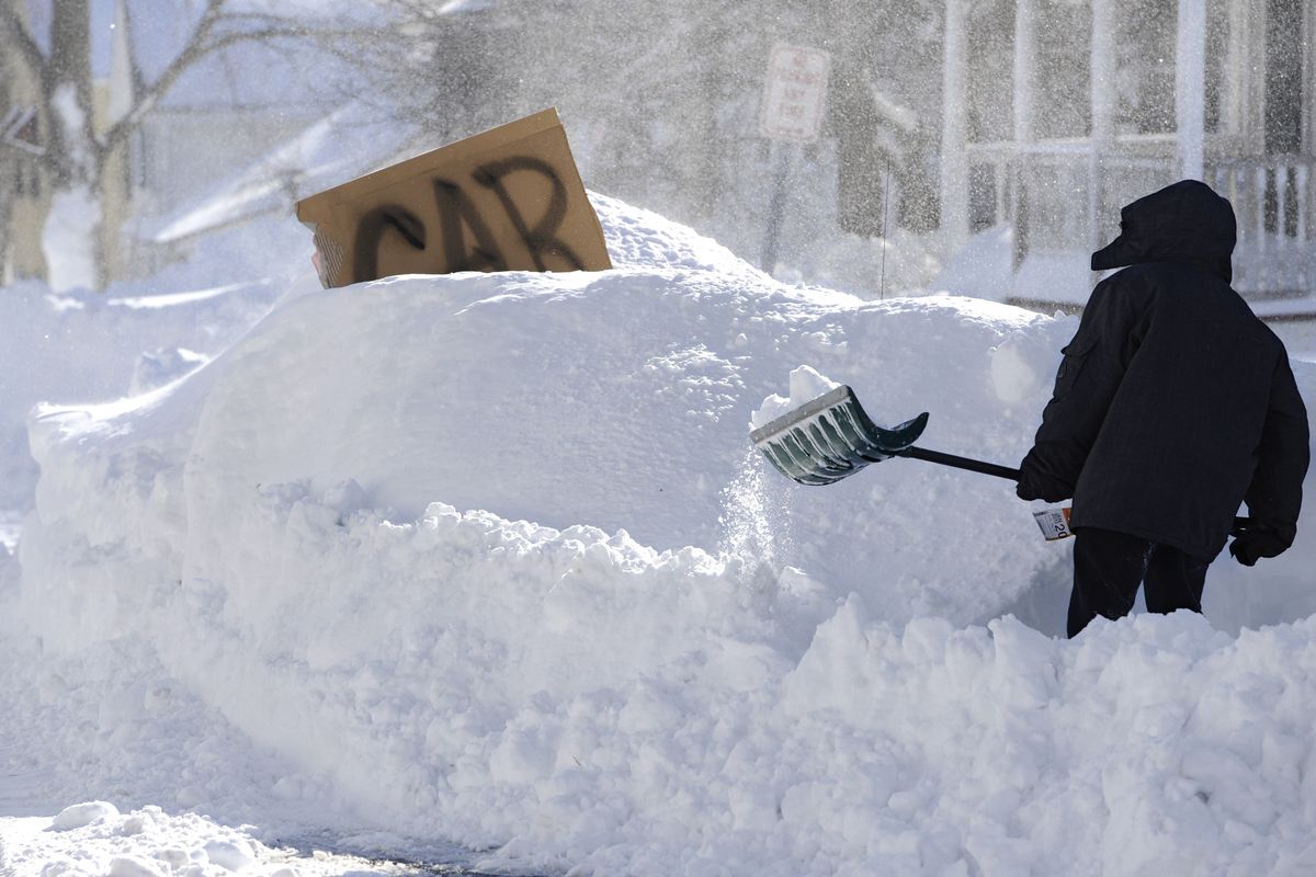 A boy shovels around a buried vehicle marked with a cardboard sign on a residential street in Windsor Locks, Conn., on Saturday. (Associated Press)