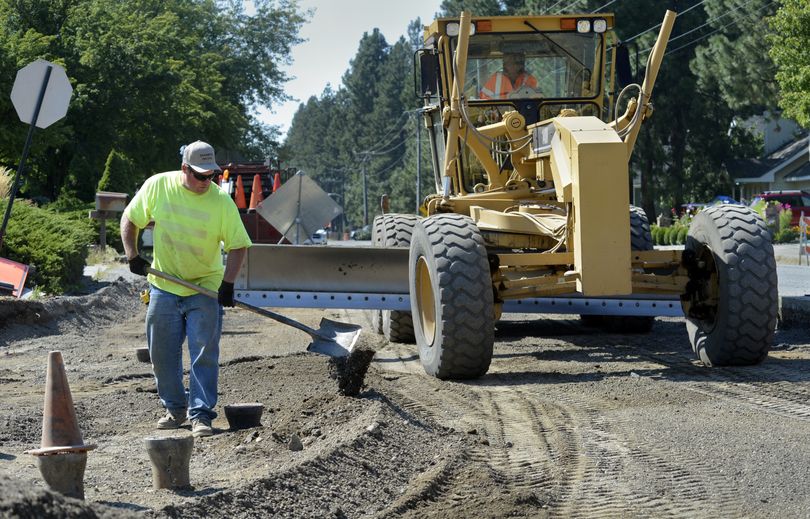 Rob Bockemuehl cleans around a water valve as a road grader prepares the intersection of 24th Avenue and Evergreen Road for paving, Monday. (Dan Pelle)