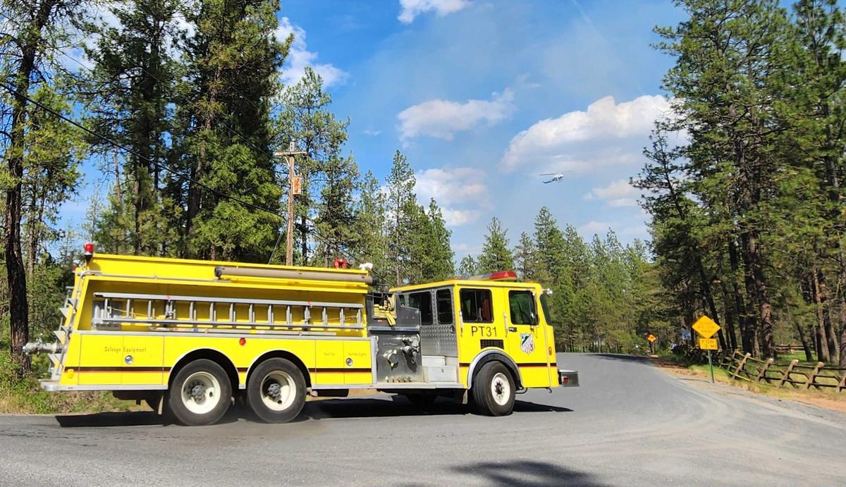 A firetruck turns towards a fire in Cheney on Saturday afternoon, while a helicopter hovers in the background.  (Cannon Barnett / The Spokesman-Review)