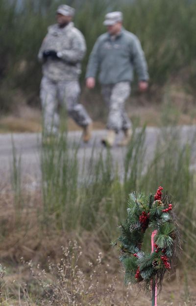 Army Lt. Col. Gary Dangerfield, left, and Chief Warrant Officer 5 James Oliphant walk down a road past a holiday wreath that was left near where two helicopters crashed Monday night. (Associated Press)