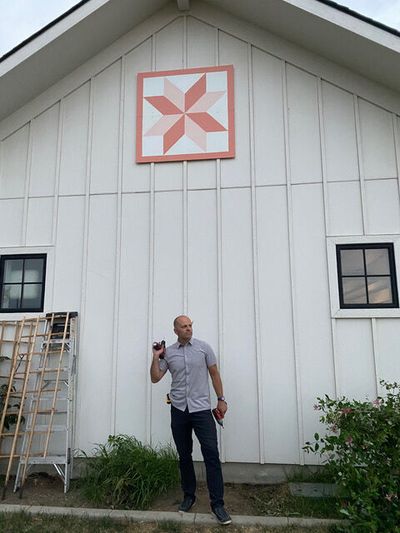 Logan Ditto poses beneath the barn quilt his wife, Julia, had painted.  (Julia Ditto)