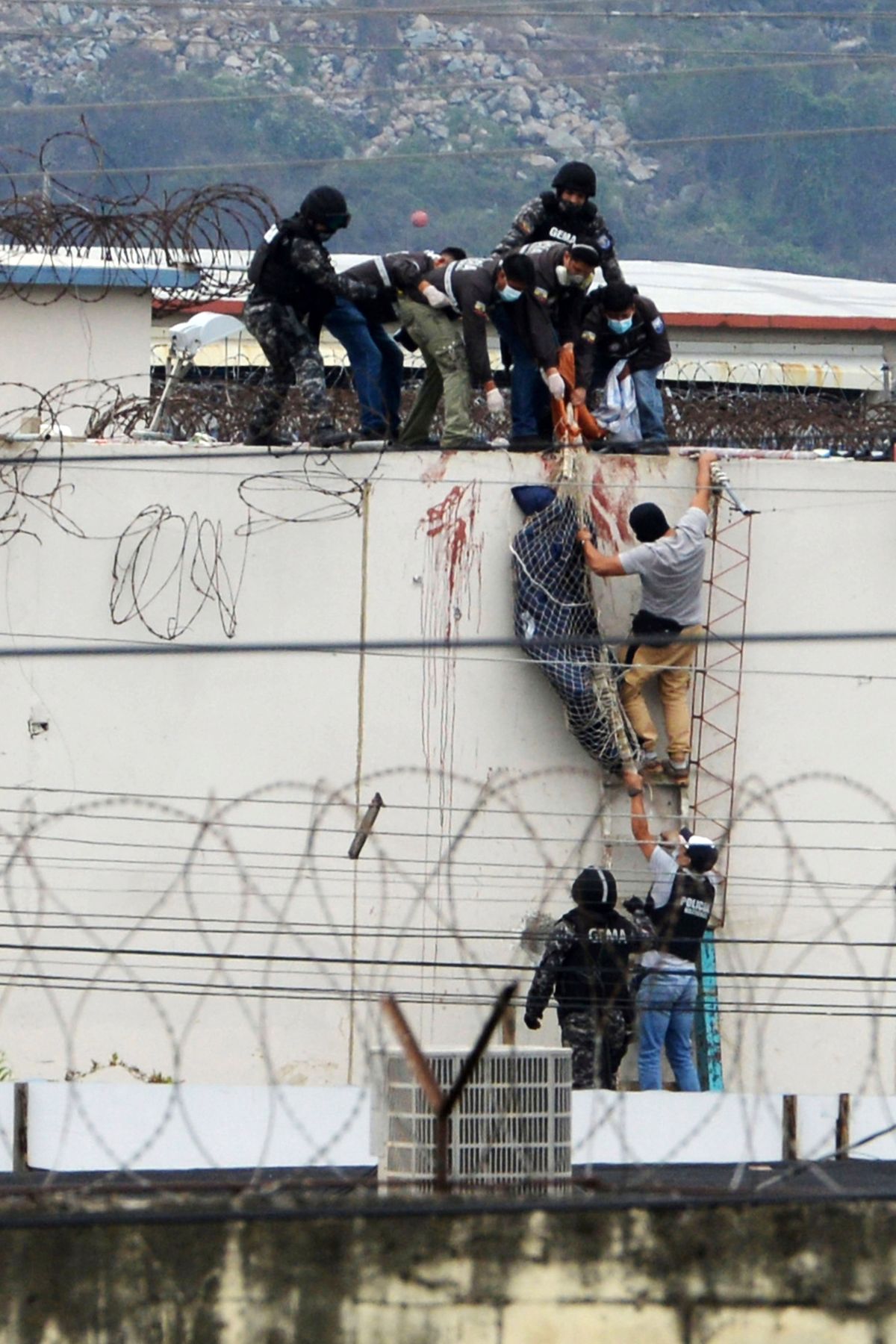 Police lower the body of a prisoner from the roof of the Litoral penitentiary the morning after riots broke out inside the jail in Guayaquil, Ecuador, Saturday, Nov. 13, 2021.  (Jose Sanchez)