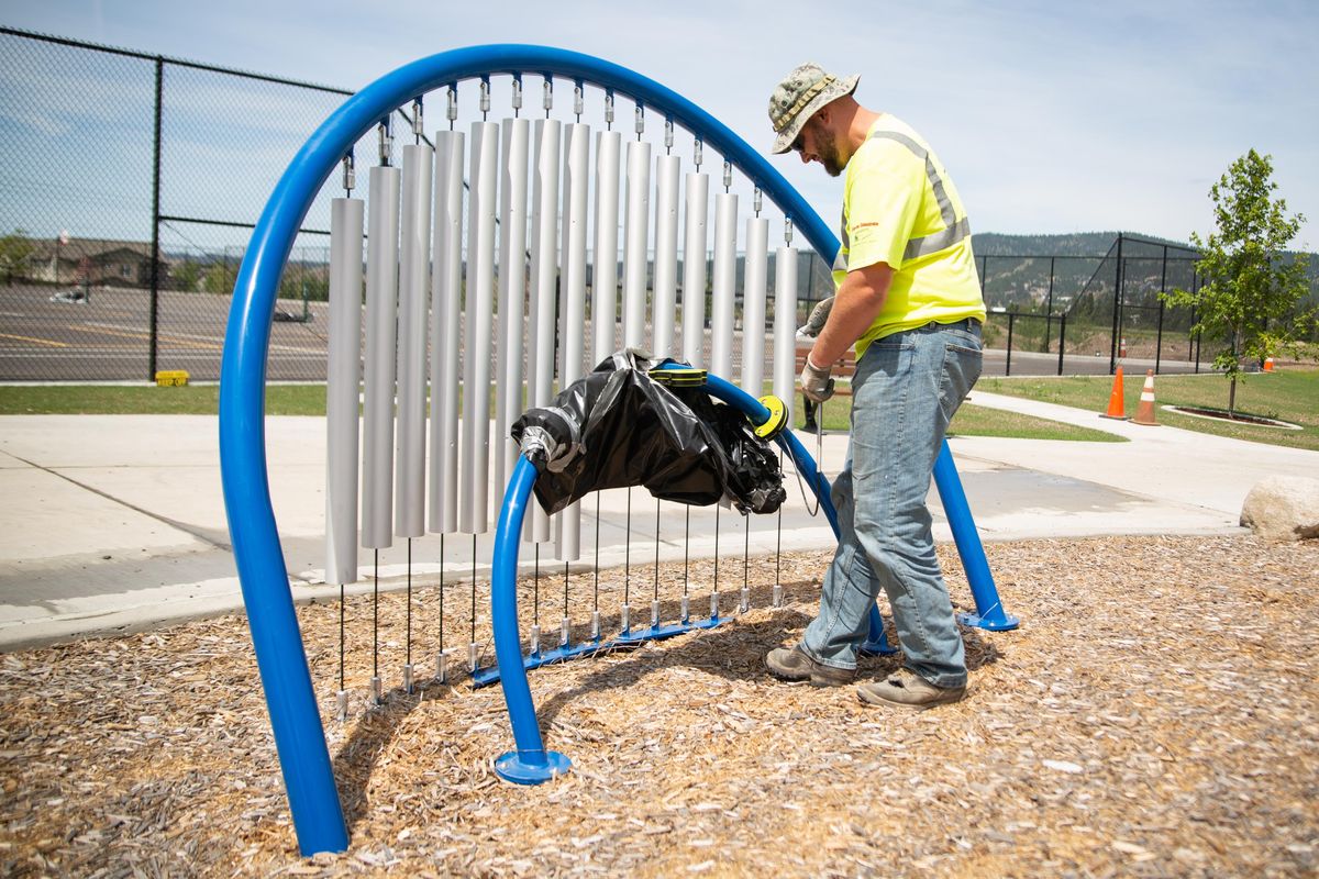 Construction worker Joel Picker of Bacon Concrete Inc. unwraps a portion of fixtures in the musical instrument area near the playground at Orchard Park in Liberty Lake, Wash. on June 10, 2019. The 11 acre park features many amenities including an 8,000 square foot splash pad, a paved recreation area that contains four tennis courts over eight pickleball courts, a tricycle path, plus covered picnic tables and restroom facilities. (Libby Kamrowski / The Spokesman-Review)