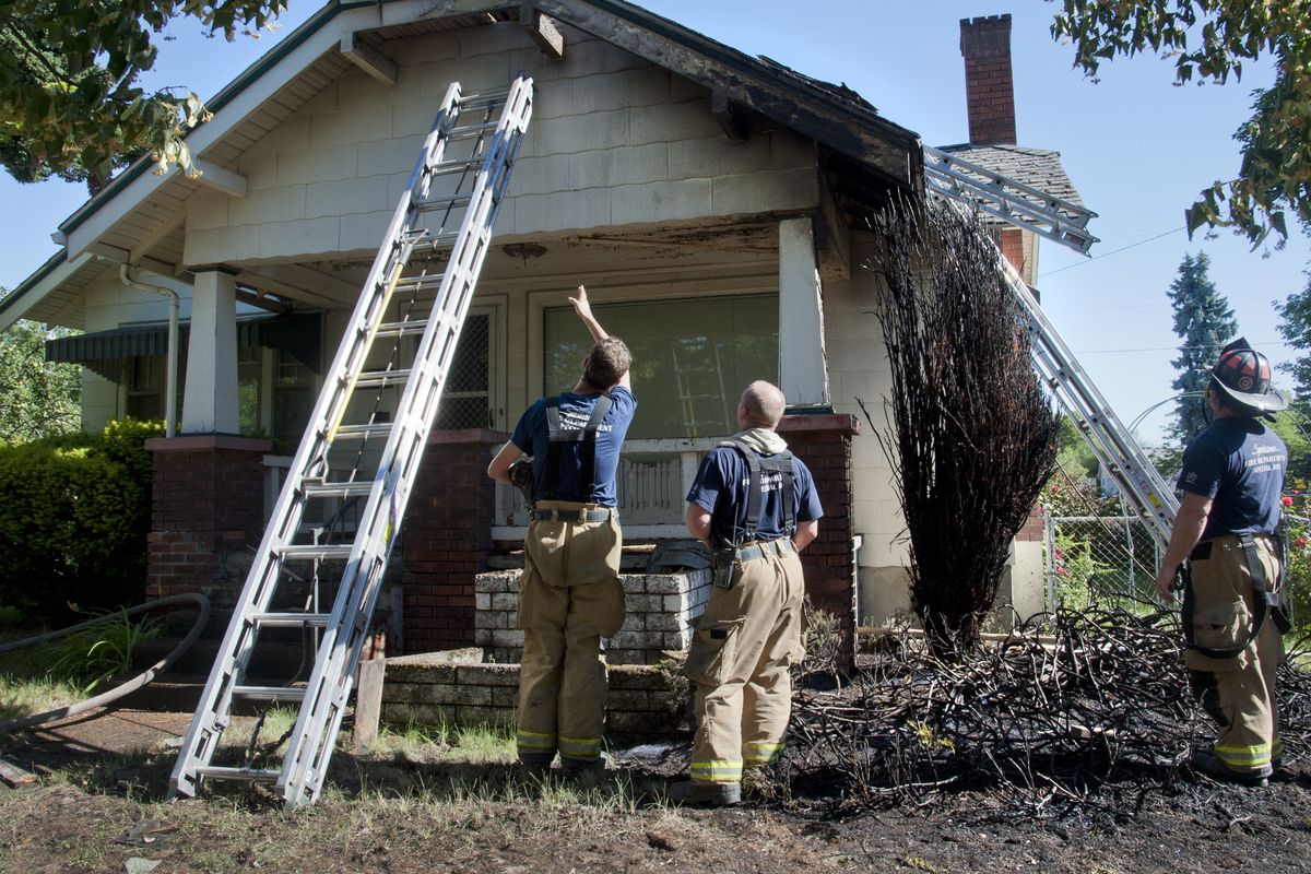 Spokane firefighters view the damage to a home at the corner of Broadway and Chestnut on Wednesday. The blaze started around the bush at right and climbed into the home