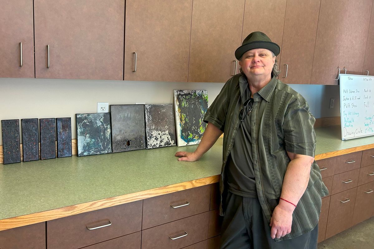 L.A. Chrisman posing in front of a series of paintings based on their grief after their partner died in 2022.  (Alexandria Osborne/For The Spokesman-Review)