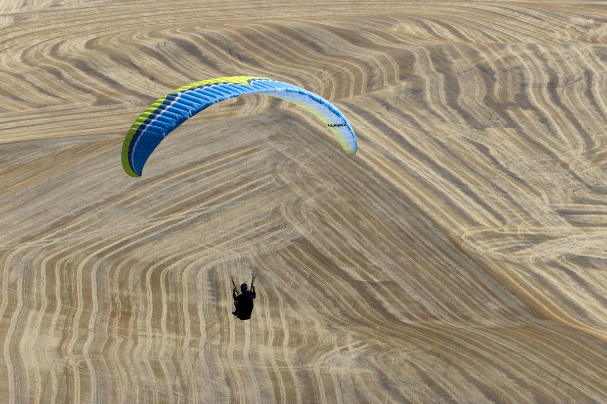 Branden Zunin of Sandpoint flies his paraglider over harvested fields after taking off from Steptoe Butte on Saturday, Sept. 9, 2023. Zunin was participating in a fly-in held to celebrate 50 years of hang gliding at Steptoe Butte. The event was organized by Center of Lift hang gliding and paragliding club in Spokane. (Geoff Crimmins/For the Spokesman-Review)