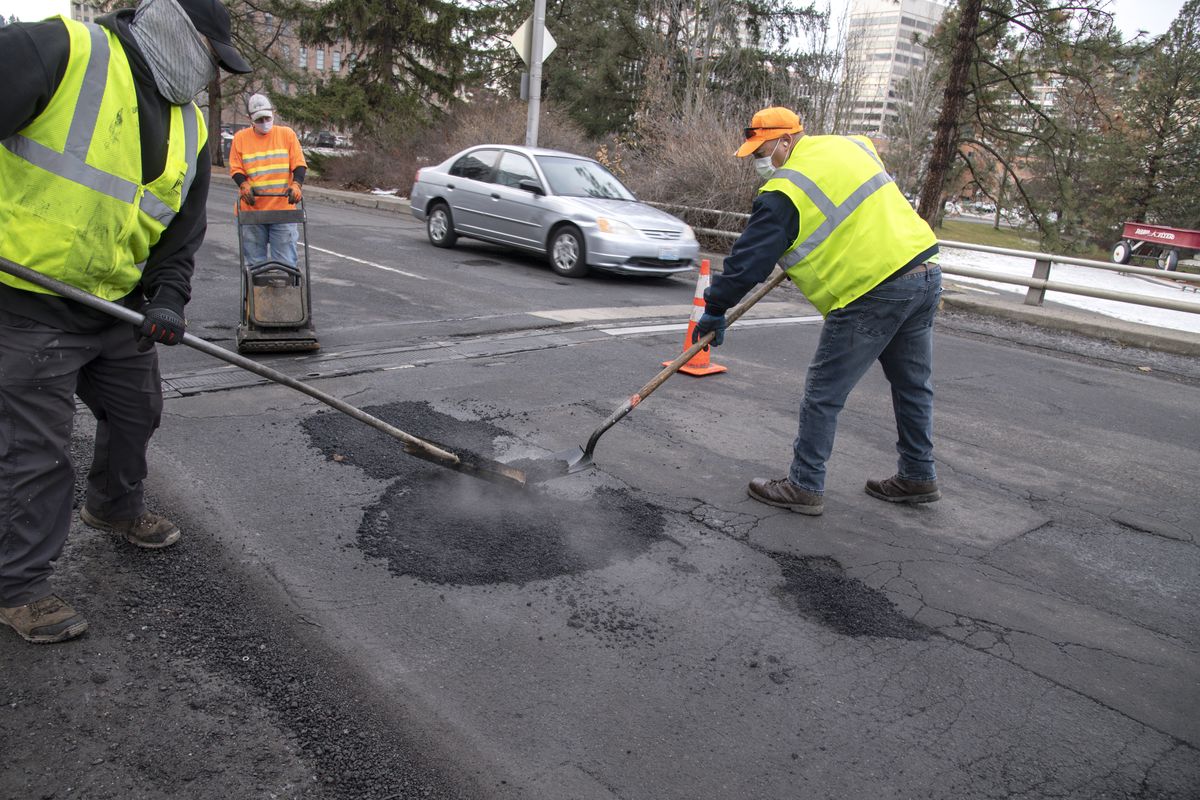 Street Department workers Tom Daves, left, Kelly Stevens, center, and Alex Mizner patch holes in the asphalt on Washington Street, north of Spokane Falls Boulevard Friday, Jan. 21, 2022. Midwinter pothole repair requires heating up cold patch materials to help it adhere to the roadway.  (Jesse Tinsley/THE SPOKESMAN-REVIEW)