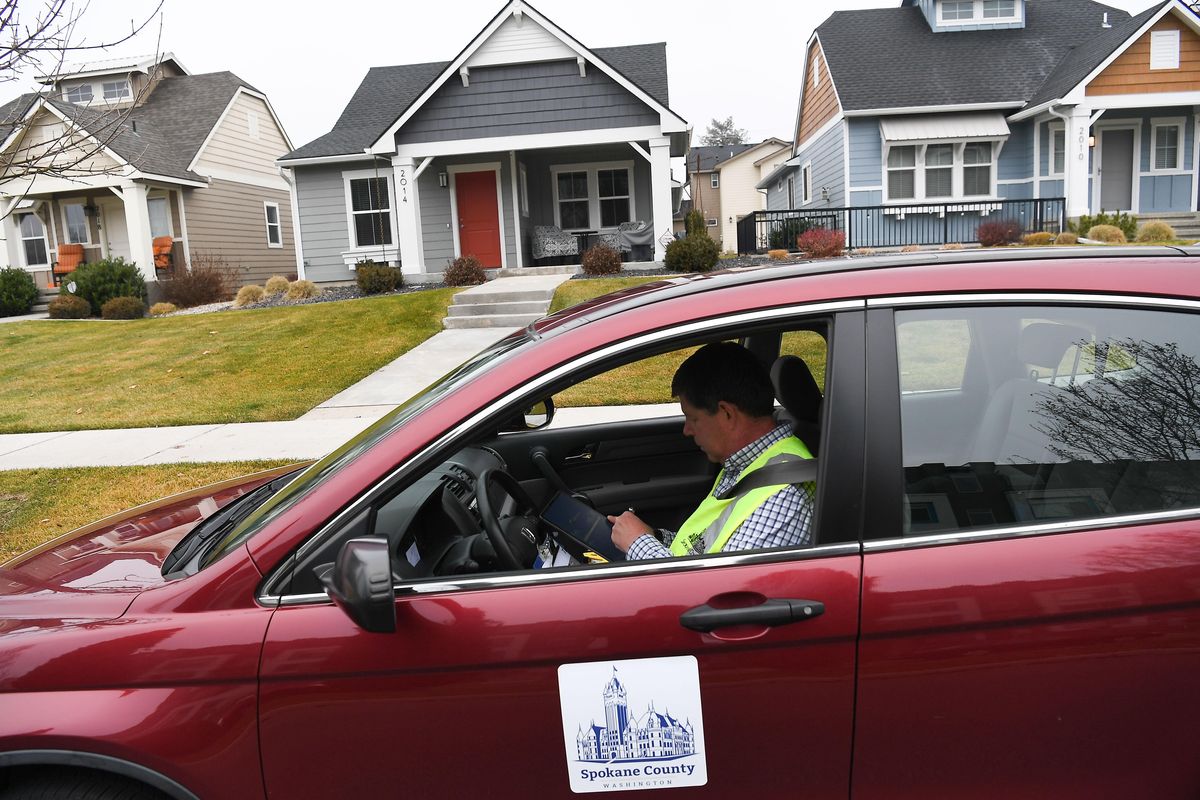 Though he normally works in Spokane Valley, assessor Steve Sanders demonstrates how he works from his personal vehicle, which is branded in Spokane County logos, as is his fluorescent green vest, in this staged photograph on Friday, Nov. 22, 2019, in Kendall Yards in Spokane. (Tyler Tjomsland / The Spokesman-Review)