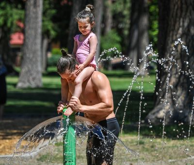 Isabella Ferderer, 3, gets her toes tickled by her father, Beau, during play at the Coeur d'Alene Park splash pad June 26 in Spokane.  (Dan Pelle/The Spokesman-Review)
