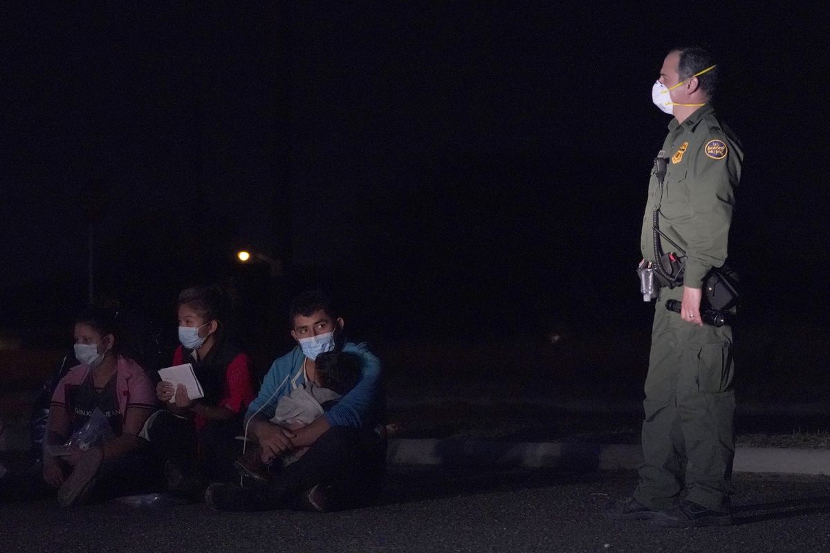 A migrant man, center, holds a child as he looks at a U.S. Customs and Border Protection agent at an intake area after crossing the U.S.-Mexico border early Wednesday in Roma, Texas. (Julio Cortez)