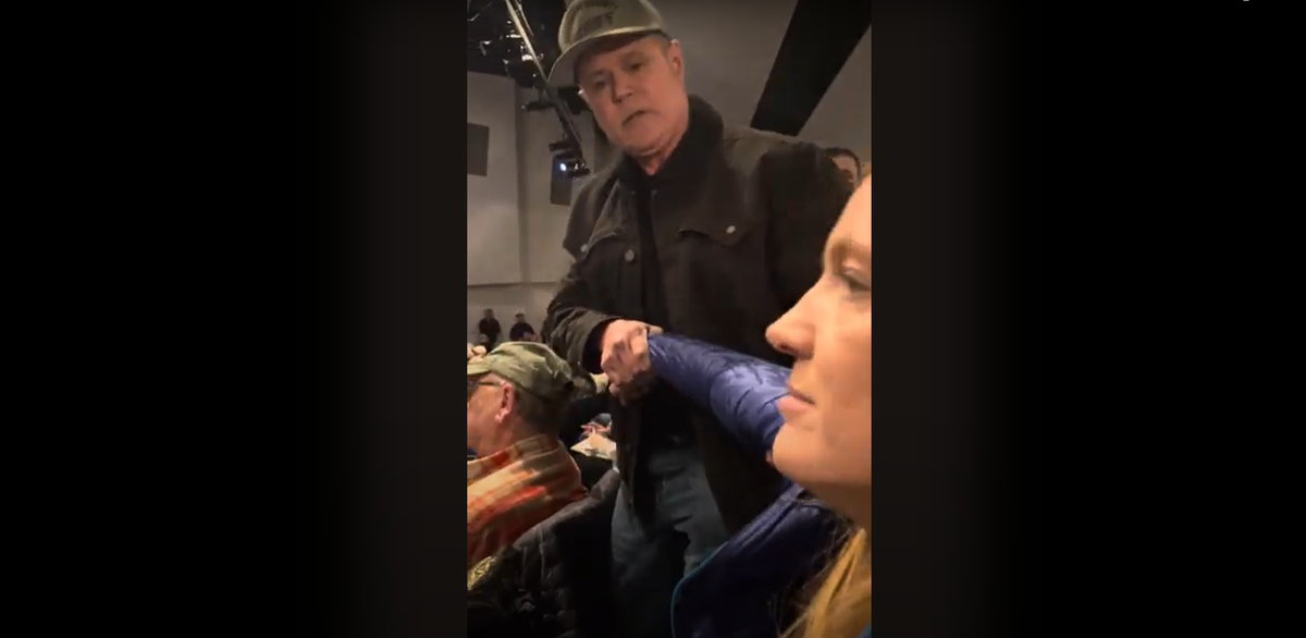 Screenshots captured from a video posted by Laura Tenneson, who sat next to Teresa Borrenpohl during the scene, show Kootenai County Sheriff Robert Norris tugging a stone-faced Borrenpohl by the arm attempting to remove her from the Coeur d’Alene High School auditorium after she interrupted a Republican town hall event on Saturday. (Screen grab)