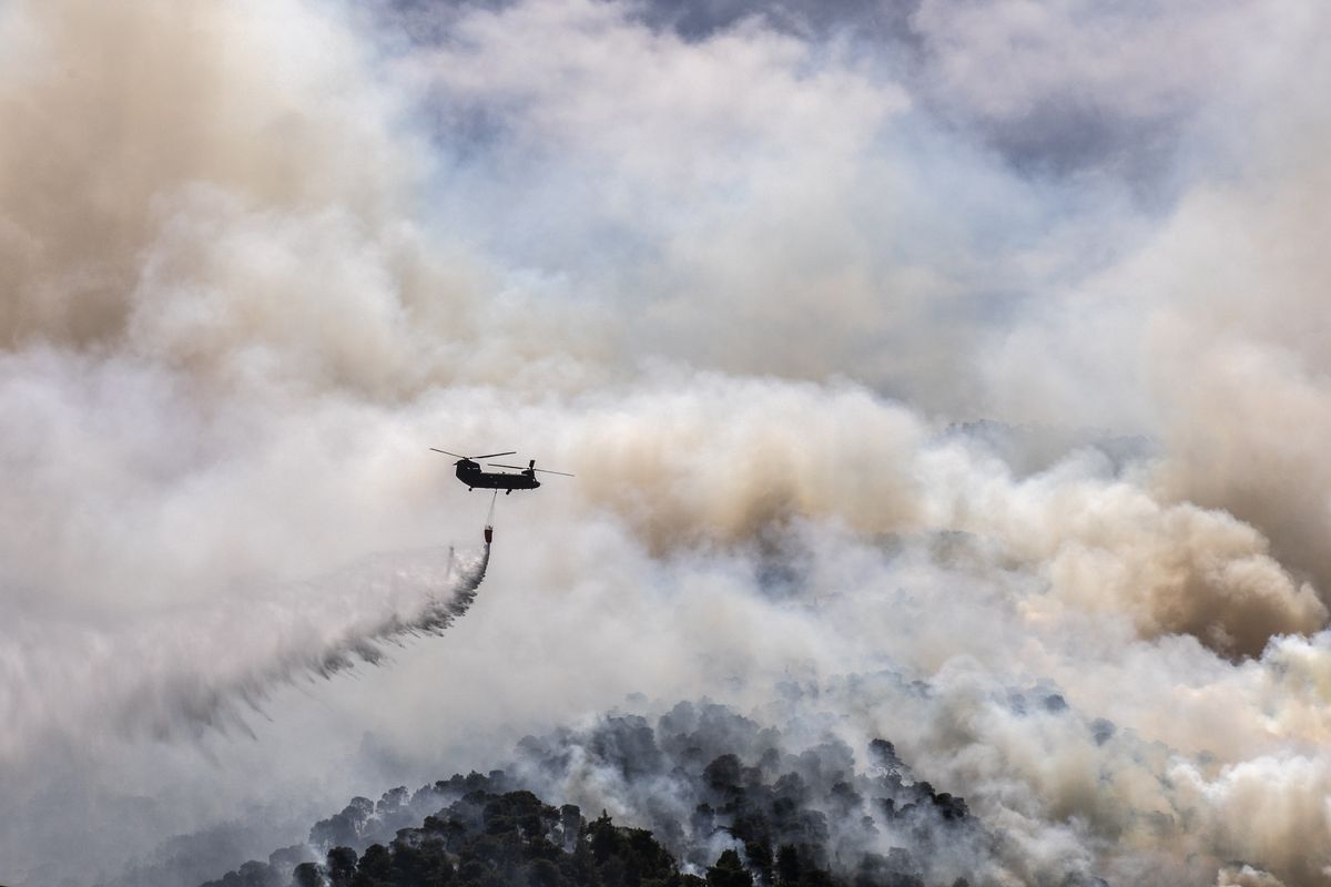 A military helicopter drops water over a forest near the village of Schinos, Corinth, Greece, on Thursday, May 20, 2021. A large wildfire west of Athens damaged homes and prompted evacuations as it tore through rugged forest terrain. Fire Service officials said eight water-dropping planes and three helicopters were involved to try and contain the blaze some 70 kilometers (45 miles) west of Athens, outside the resort town of Loutraki. (Petros Giannakouris)