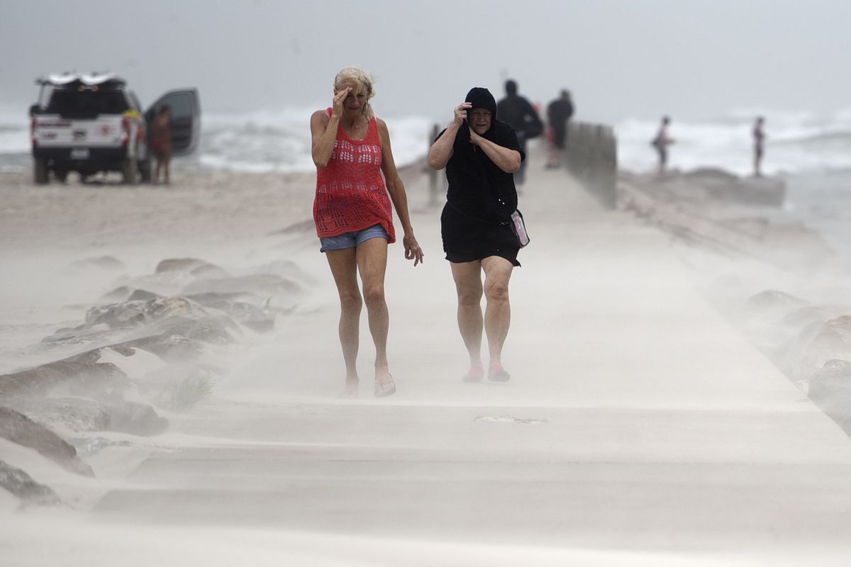 People shield their faces from wind and sand ahead of Tropical Storm Nicholas, Monday, Sept. 13, 2021, on the North Packery Channel Jetty in Corpus Christi, Texas. Lifeguards paroled the beach to warn people of the upcoming conditions.  (Annie Rice)