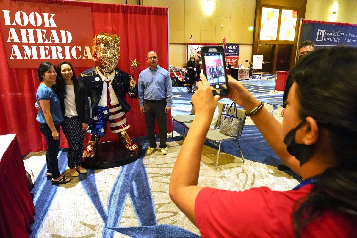 Conference attendees pose for a photo next to a statue of former president Donald Trump at the merchandise show at the Conservative Political Action Conference (CPAC) Saturday, Feb. 27, 2021, in Orlando, Fla.  (John Raoux)