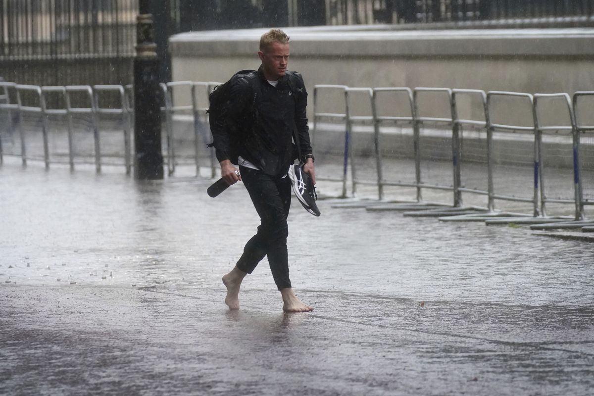 A man walks in bare feet through flood water in Horse Guards Road in central London, Sunday July 25, 2021. Thunderstorms bringing lightning and torrential rain to the south are set to continue until Monday it is forecast.  (Victoria Jones)