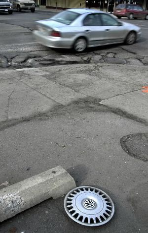 A northbound car passes over a section of broken pavement at the corner of 3rd and Washington in 2003 as a lost hubcap lies a few feet from the damaged road.  (Dan Pelle)