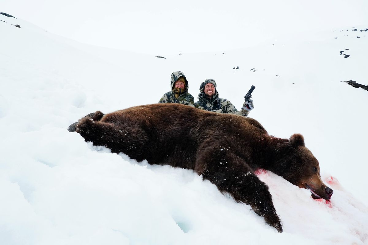 Trevor Schneider and Tana Grenda sit by the coastal brown bear that nearly killed them on May 13, 2021 in Alaska.  (Courtesy of Trevor Schneider)