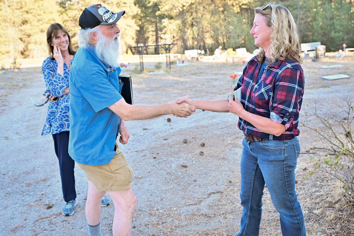 Elk Cemetery challenger Steven Queener, left, shakes hands with incumbent Commissioner Rebecca Shannon as Queener’s campaign health care consultant Dr. Bernadine Bank smiles Wednesday at Elk Cemetery. (Tyler Tjomsland/The Spokesman-Review)