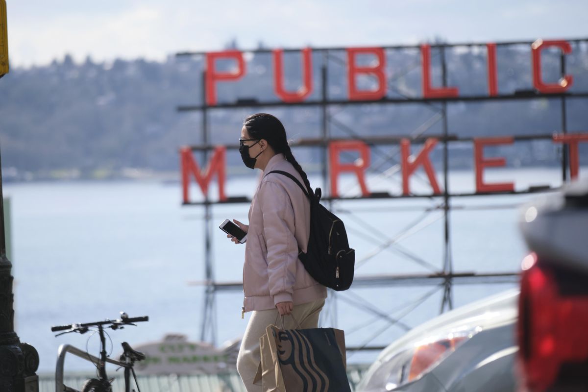 A person wearing a mask crosses the street in front of the Pike Place Public Market, an area tourist attraction, on Wednesday, March 11, 2020, in Seattle. In efforts to slow the spread of the new coronavirus, Washington state Gov. Jay Inslee announced a ban on large public gatherings in three counties in the metro Seattle area. (Stephen Brashear / Associated Press)