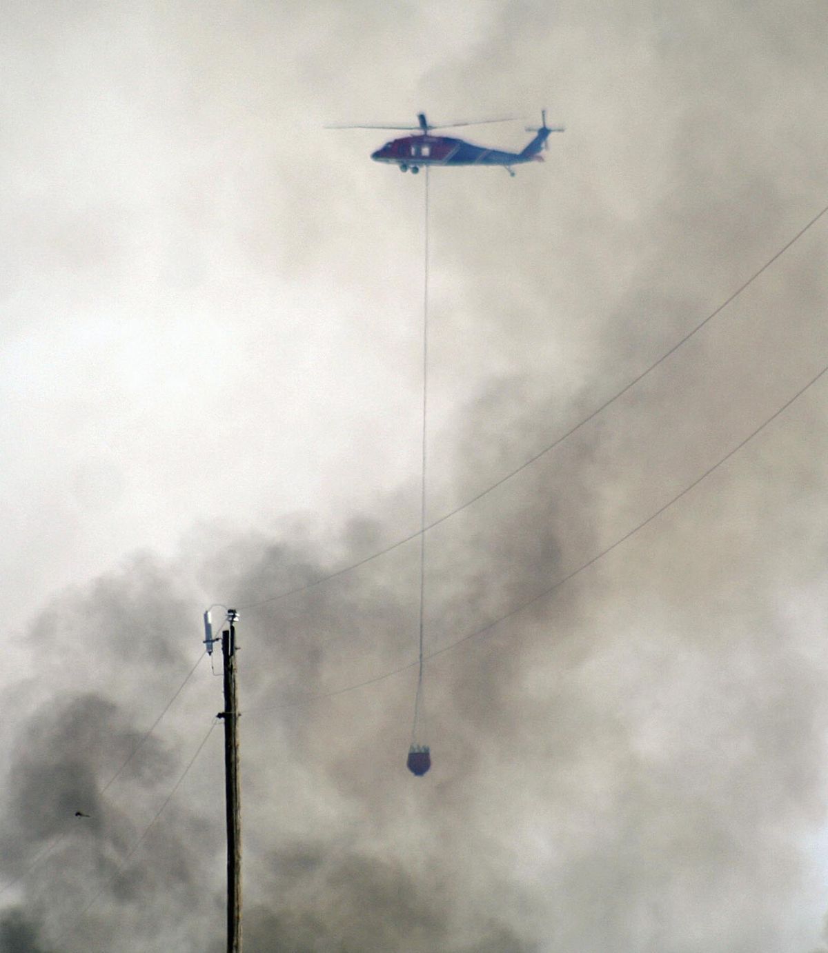 A helicopter moves in through smoke to drop water on a wildfire Friday, April 13, 2018, north of Woodward, Okla. A wildfire in northwestern Oklahoma has burned more than 120,000 acres and forced hundreds of people to evacuate their homes. (Rachael Van Horn / AP)