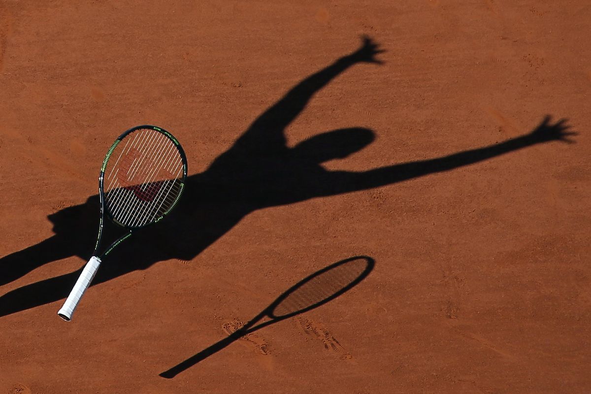 Serena Williams casts a shadow on the clay as she drops her racket while celebrating winning the final of the French Open on June 6, 2015.  (David Vincent)