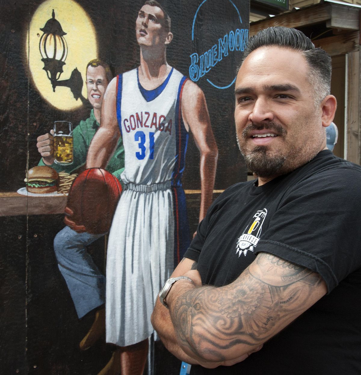 Scotty’s Doghouse general manager, Joey LaRocque, stands Friday in front of the newly installed mural on the business’ north side. Owner Scott Wilburn is depicted in the green shirt at left next to  Gonzaga University basketball player Casey Calvary. (Dan Pelle / The Spokesman-Review)