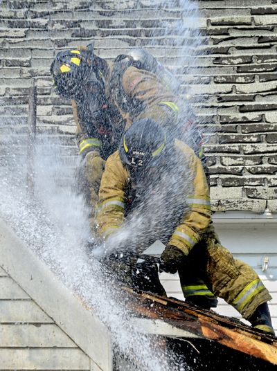 Fighting a house fire: Spokane firefighters from Station 2 try to ax through the roof of an unoccupied house as the spray from a fire hose from inside the house blasts them at 554 E. Lacrosse Ave. in Spokane on Wednesday. The fire started in the yard’s tall, dry grass and spread around the house. Burning embers started the roof on fire. The cause is under investigation. (Dan Pelle)