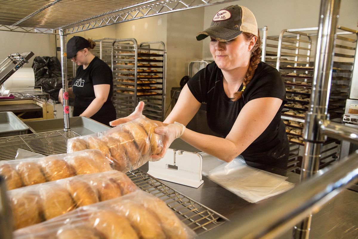 Sarah Donaldson places a fresh half-dozen cheese bagels that have been sealed into plastic onto a rack at River City Kitchen on April 15 in downtown Spokane. River City Kitchen, owned by Clay Cerna, has pitched in to the Spokane food scene’s COVID-19 relief with bagels priced at 50% for customers, as well as a “bagel loan” for those who cannot afford the product at the moment. And for businesses, he has offered free space in the industrial downtown kitchen through June. (Libby Kamrowski / The Spokesman-Review)