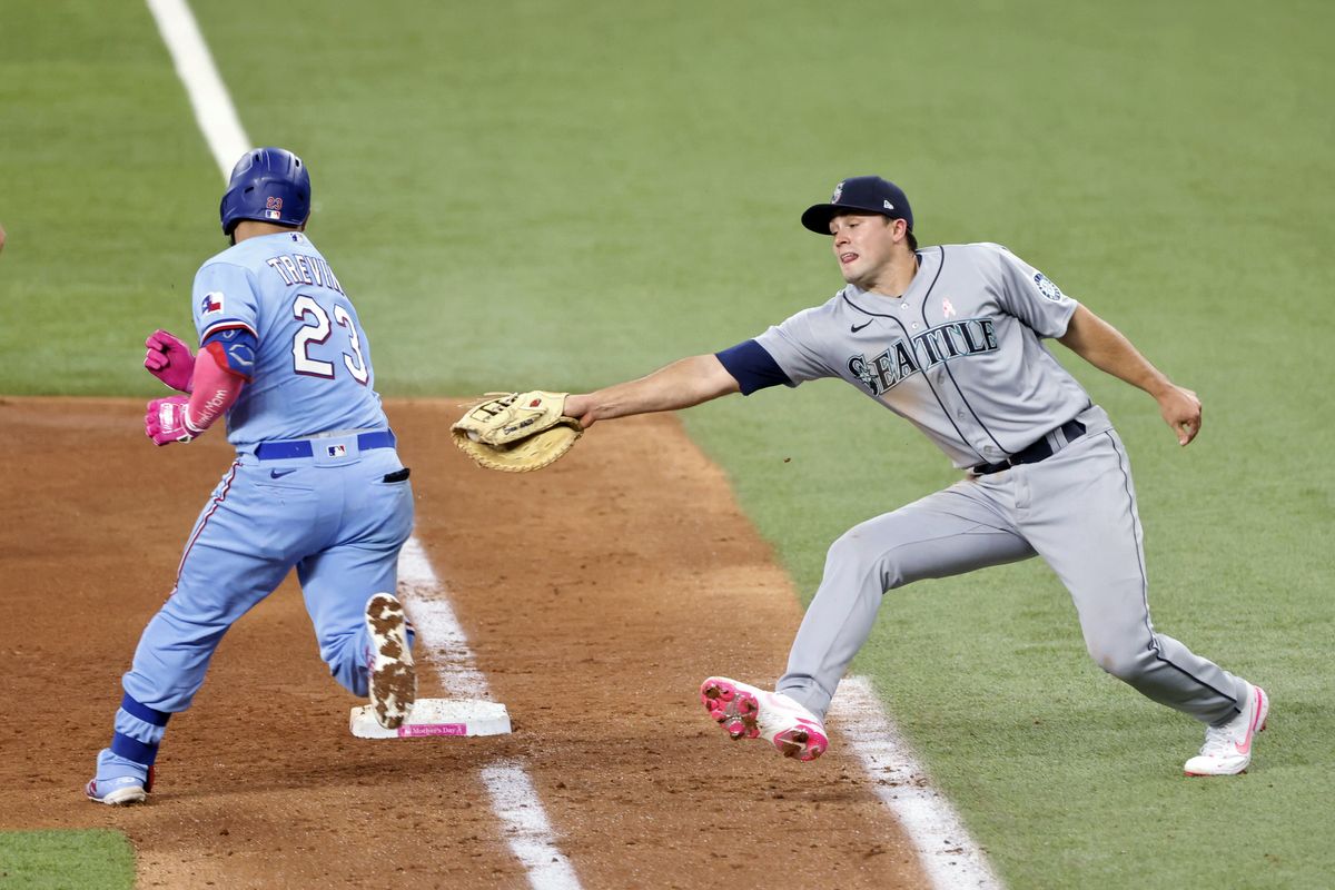 Texas Rangers catcher Jose Trevino (23) evades a tag by Seattle Mariners first baseman Evan White (12) as he makes it safely to first during the fifth inning of a baseball game Sunday, May 9, 2021, in Arlington, Texas.  (Michael Ainsworth)