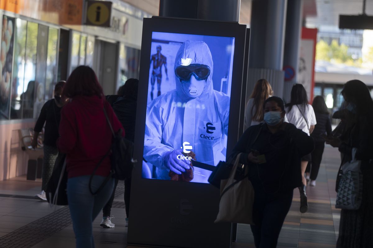 People pass by a poster thanking medical workers at a bus station in Madrid, Spain, Wednesday, Oct. 7, 2020. About 5.2 million people in Spain, including nearly 4.8 million residents in or around Madrid, are under restrictions on movement due to the second wave of the coronavirus pandemic.  (Paul White)