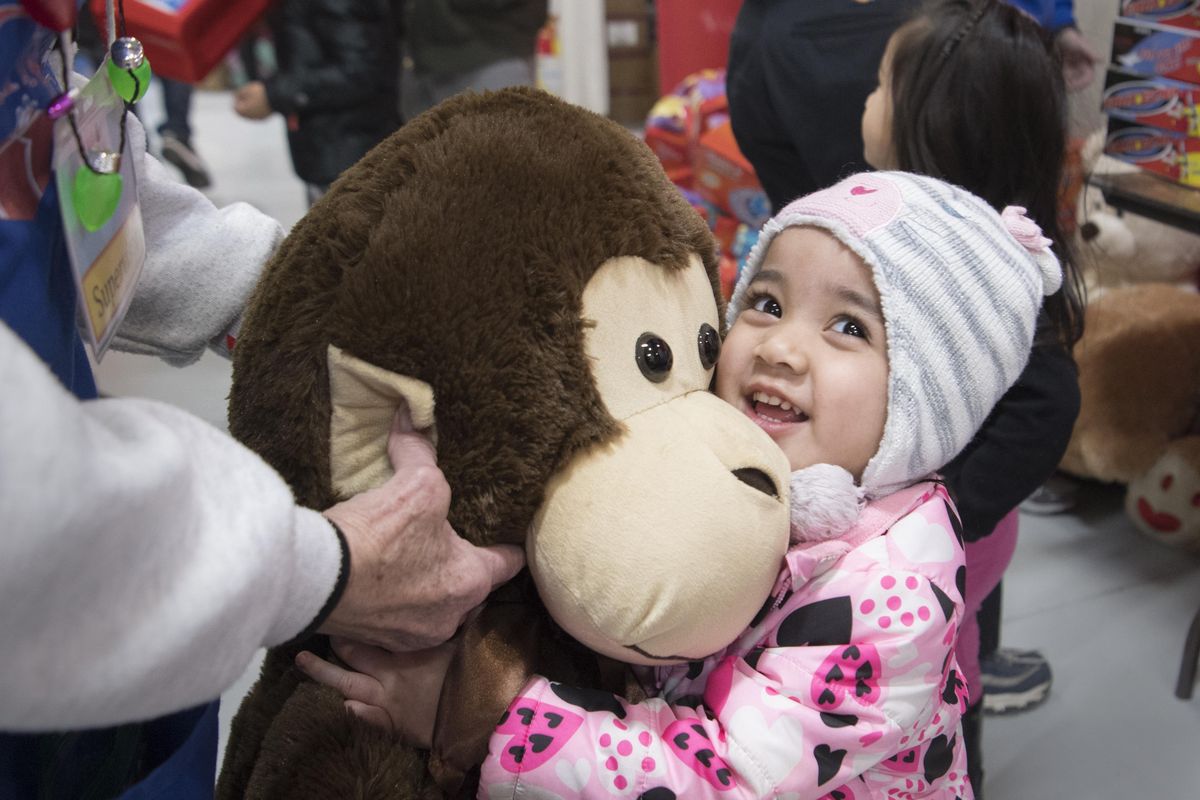 Alycia Moreang, age 2, squeezes a giant stuffed monkey, offered by Christmas Bureau volunteer Joan Haynes Wednesday, Dec. 13, 2017 at the annual charity run by Catholic Charities and the Volunteers of America. The stuffed toys come from the annual Teddy Bear Toss, which was Saturday, Dec. 9, 2017 at the Chiefs hockey game. (Jesse Tinsley / The Spokesman-Review)
