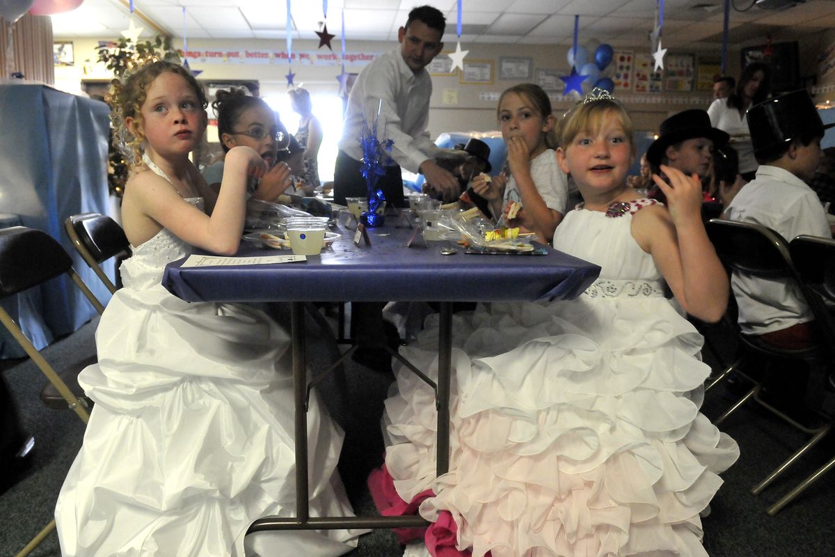 Third-graders Audrina Gainey, left, and Stephanie Sawchuk, right, wear ball gowns and munch on a lunch served by parents and teachers May 24, at Sunrise Elementary. The event, called the Fairy Tale Ball, was a time to dress up and practice proper dining etiquette. (Jesse Tinsley)
