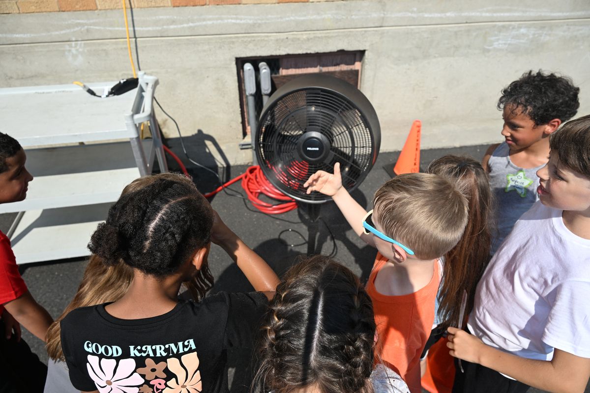 Madison Elementary School students, including second-grader David Key, in sunglasses, gather around an oscillating misting fan outside on the playground during recess to cool off Tuesday, Sept. 2, 2025, on the first day of school in the Spokane school district. Temps neared 100 degrees, and many classrooms were above 80 degrees inside. Madison is one of the older schools that doesn’t have air conditioning.  (Jesse Tinsley/THE SPOKESMAN-REVIEW)