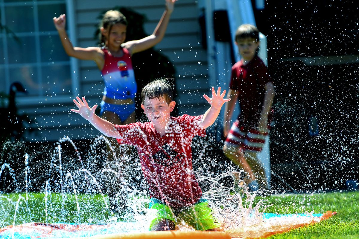 Seven-year-old Beau Jurgens, front, slides into the water while his neighbor Ellie Cordill, 8, and brother Owen Jurgens, 9, find a way to stay cool during the 105 degree weather in Liberty Lake on June 28. On June 27, Spokane reached an all-time high temperature of 109 degrees, breaking the long-standing record of 108 set in August 1961.  (Kathy Plonka/The Spokesman-Review)