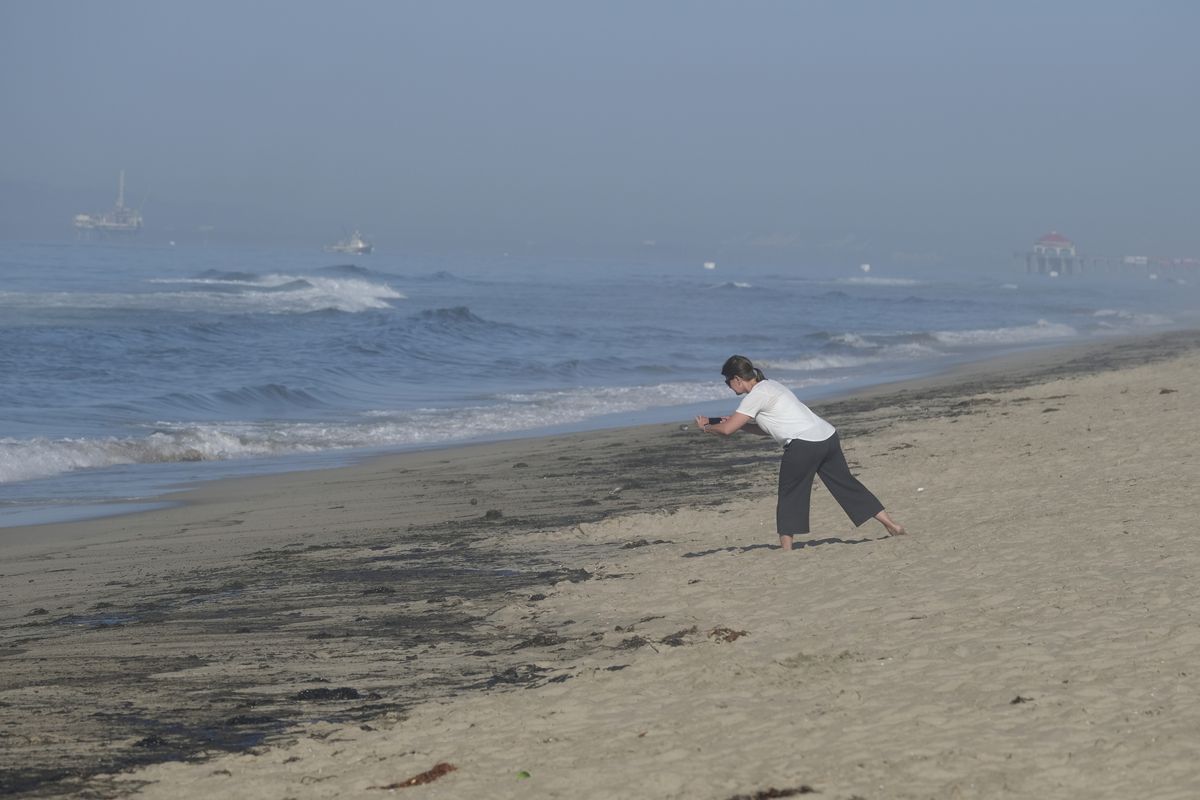 A woman takes a picture of oil washed up on Huntington Beach, Calif., Sunday., Oct. 3, 2021. A major oil spill off the coast of Southern California fouled popular beaches and killed wildlife while crews scrambled Sunday to contain the crude before it spread further into protected wetlands.  (Ringo Chiu)